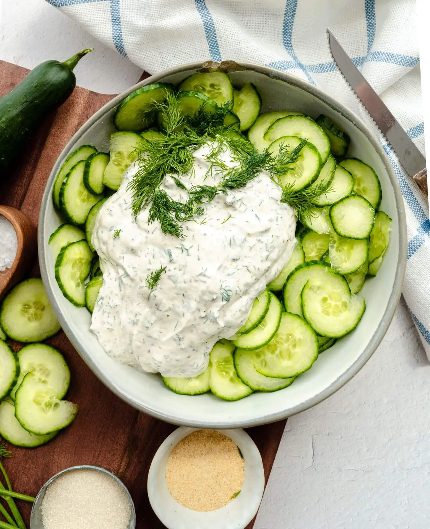 A dressing on top of thinly sliced cucumbers, not fully mixed.