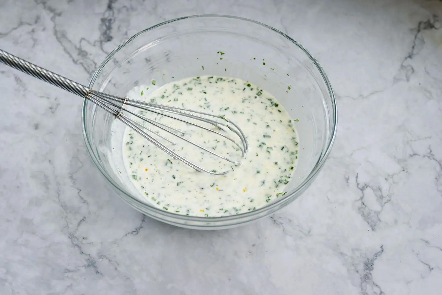 Ingredients that are needed to make kefir ranch dressing whisked together in a bowl.