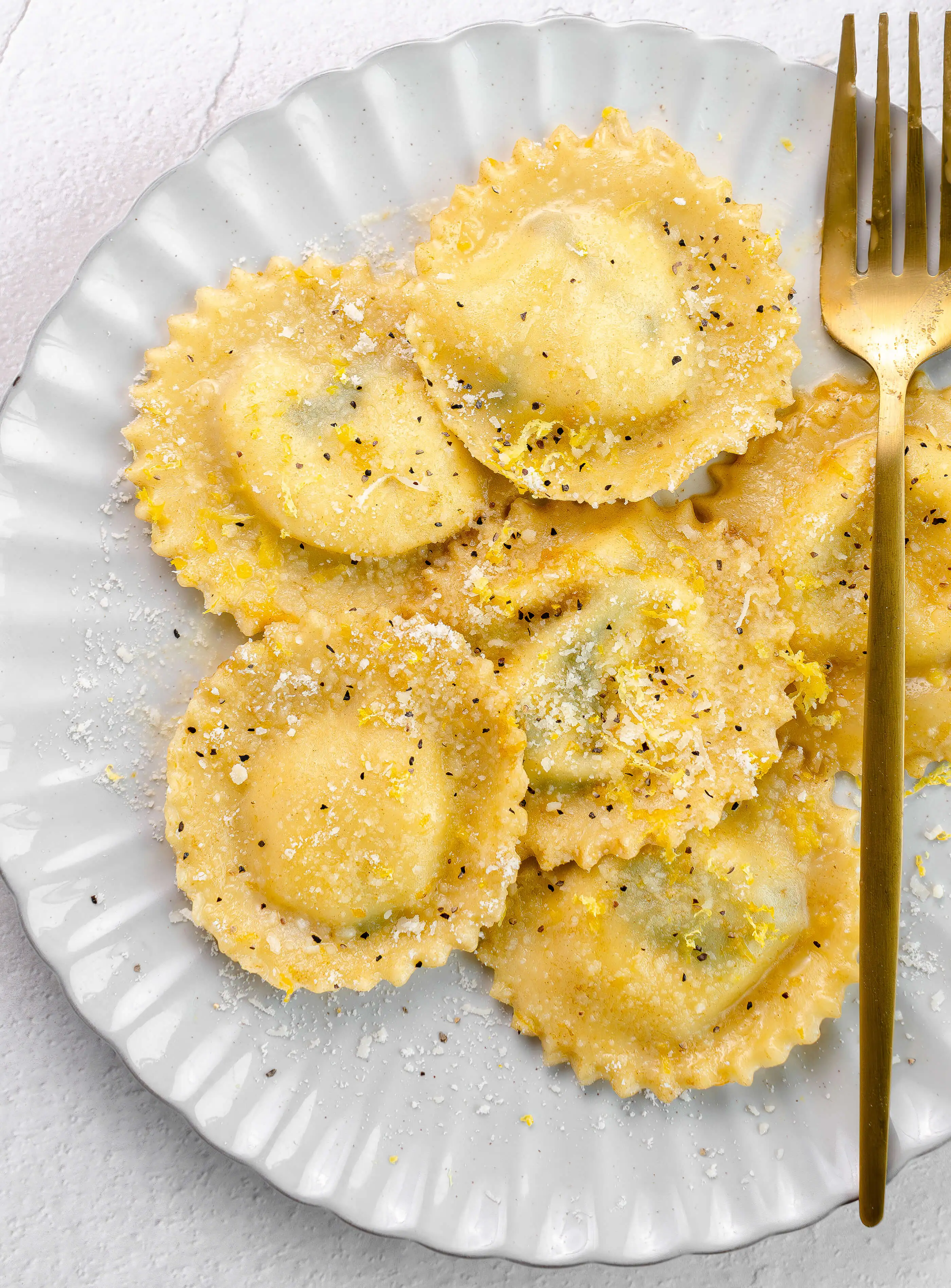 A half dozen garnished Homemade Spinach and Ricotta Ravioli ready to serve on a white plate.