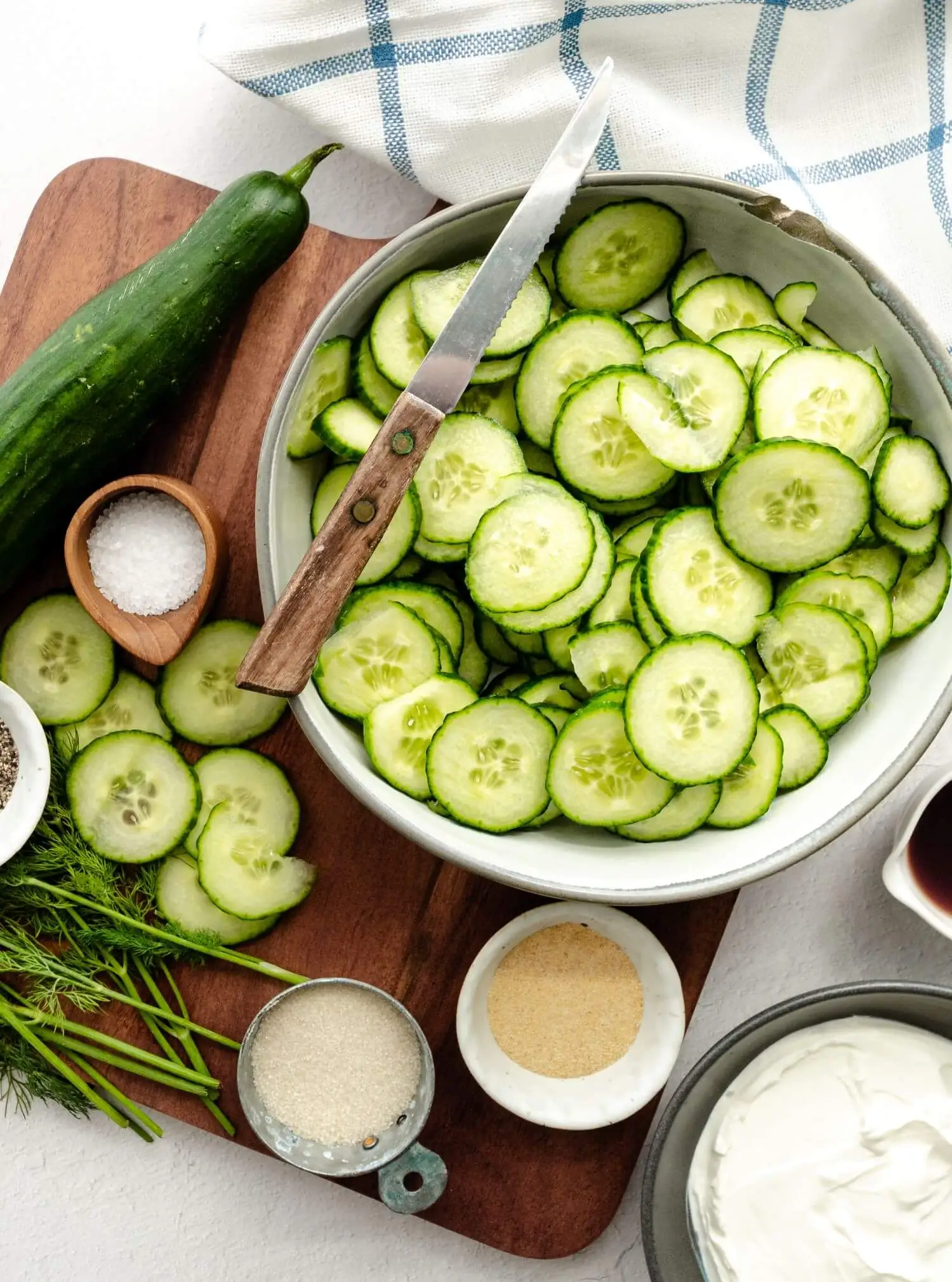 Thinly sliced cucumbers in a bowl, with a knife resting on the same bowl.