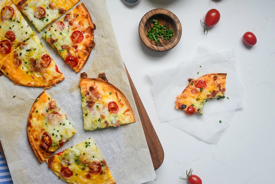Slices of crispy bacon, egg & cheese breakfast pizza on a serving board, with one slice partially eaten.