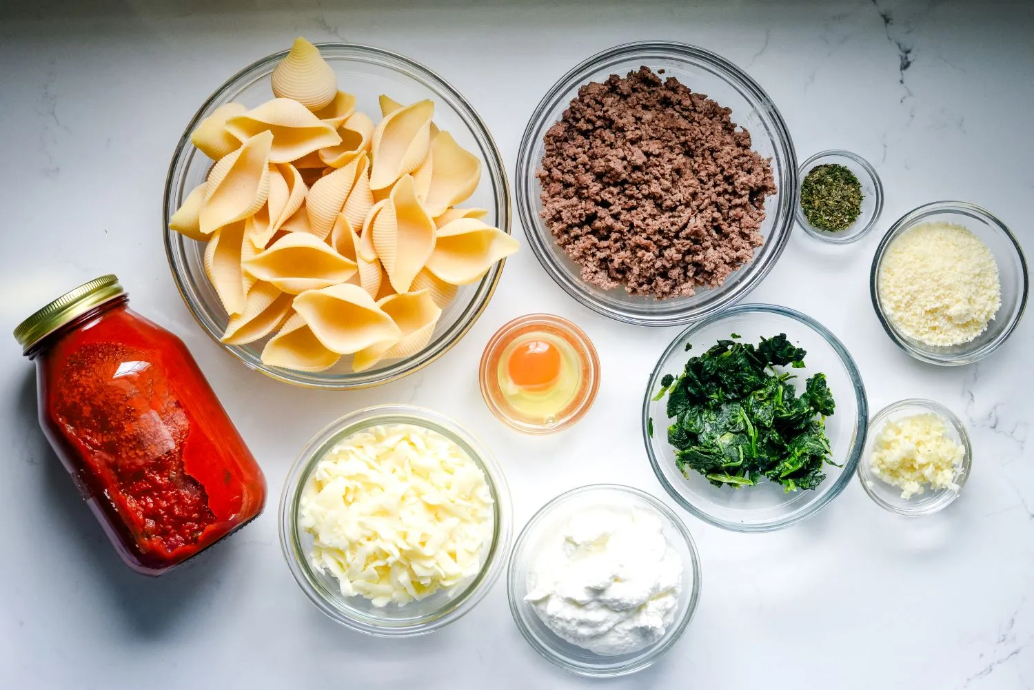 Ingredients for stuffed shells including jumbo pasta shells, ground beef, tomato sauce, ricotta cheese, and Parmesan cheese.
