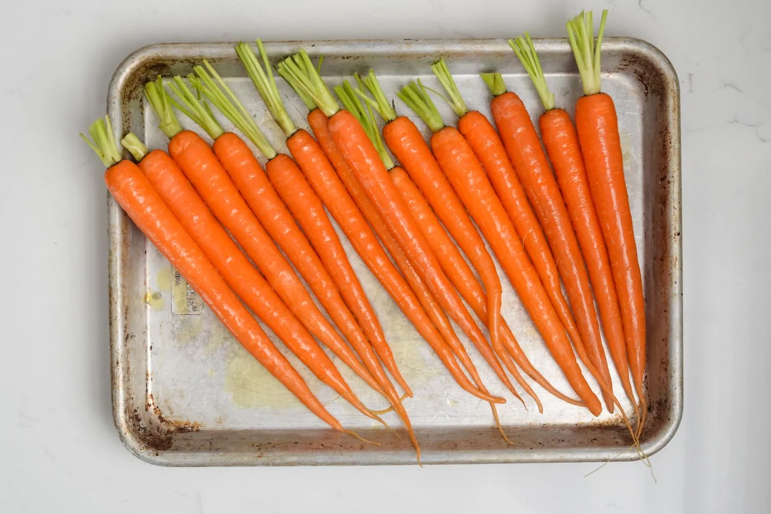Carrots tossed with olive oil on a sheet pan.