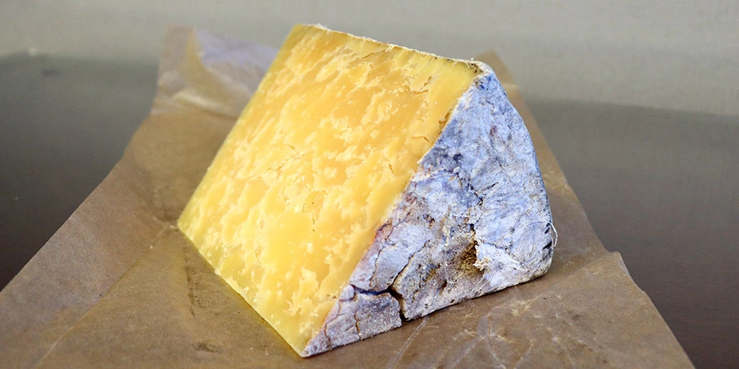 A piece of Cheddar cheese with a cloth rind presented on parchment paper.