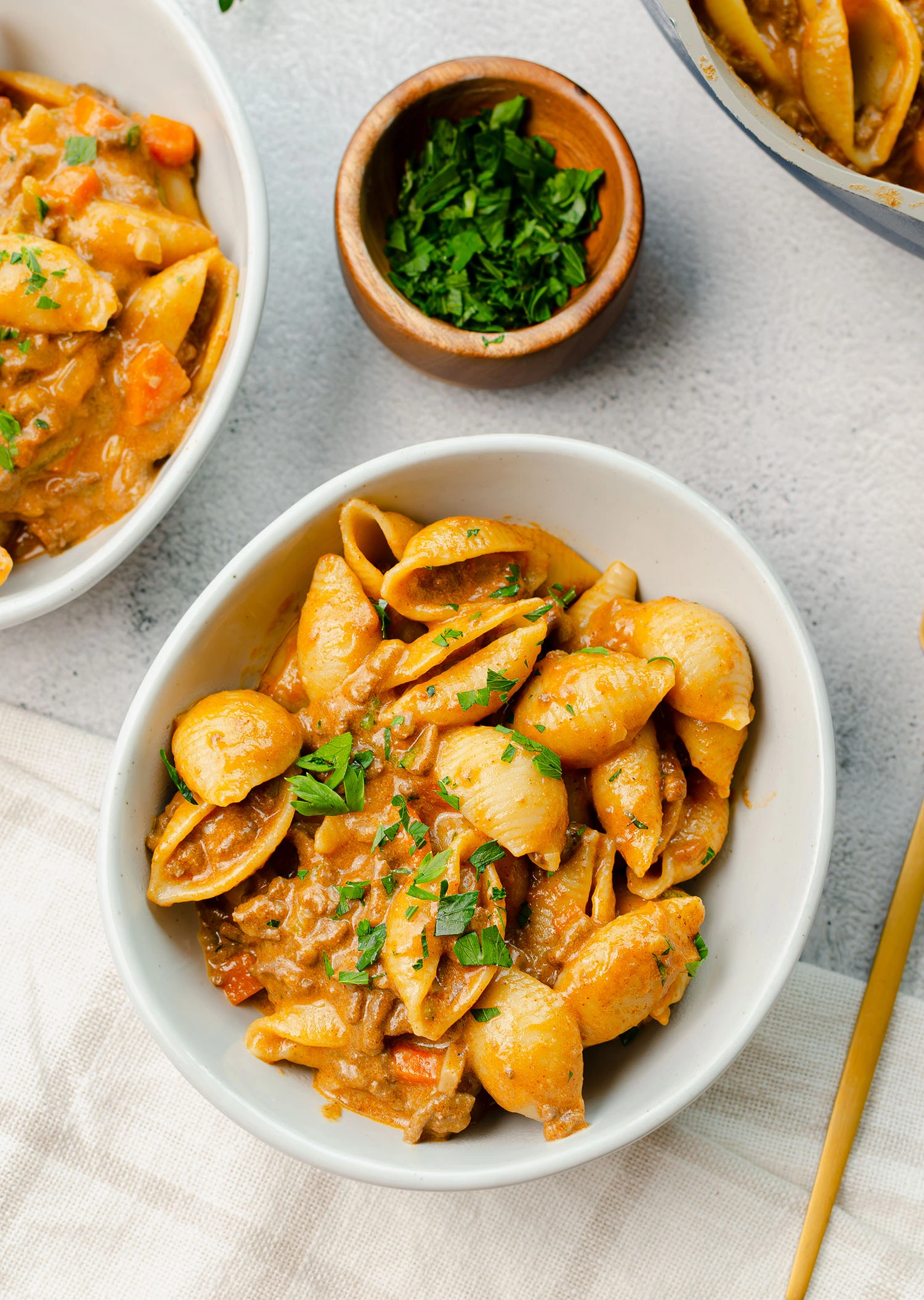 A completed hamburger veggie pasta dish featuring ground beef, carrots, onion, mushroom, zucchini, and cheddar cheese in a bowl garnished with fresh parsley, ready to be served.