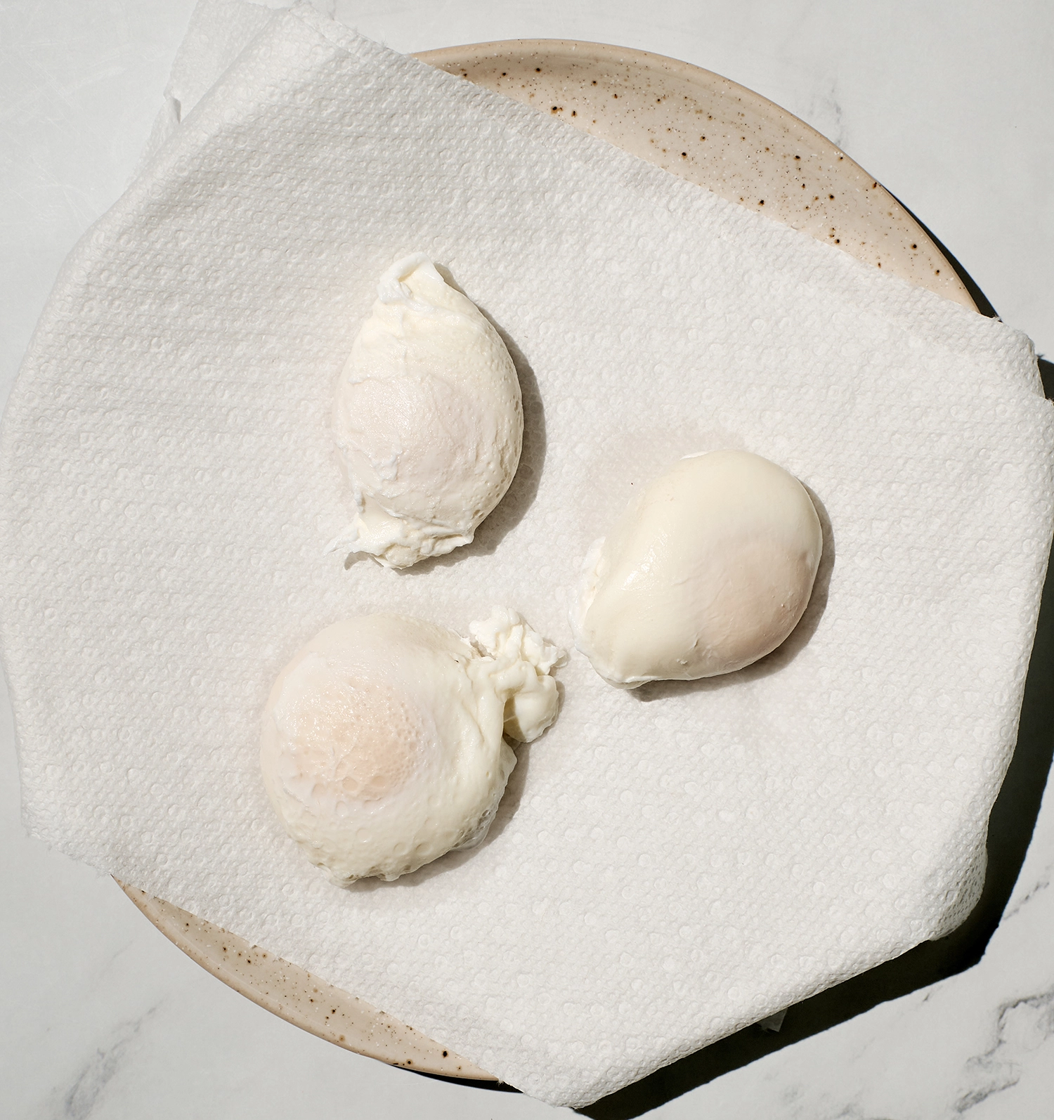 Three poached eggs rest on a paper towel placed on a plate.