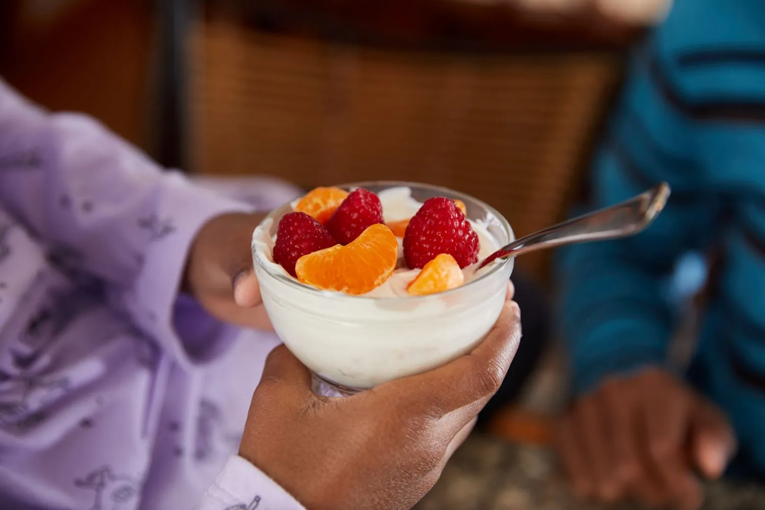 A child holds a bowl of yogurt with raspberry and mandarin topping.