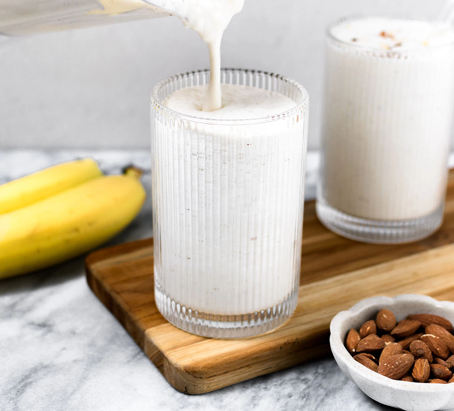 Nutritious banana smoothie with vanilla yogurt and almonds poured into a glass.