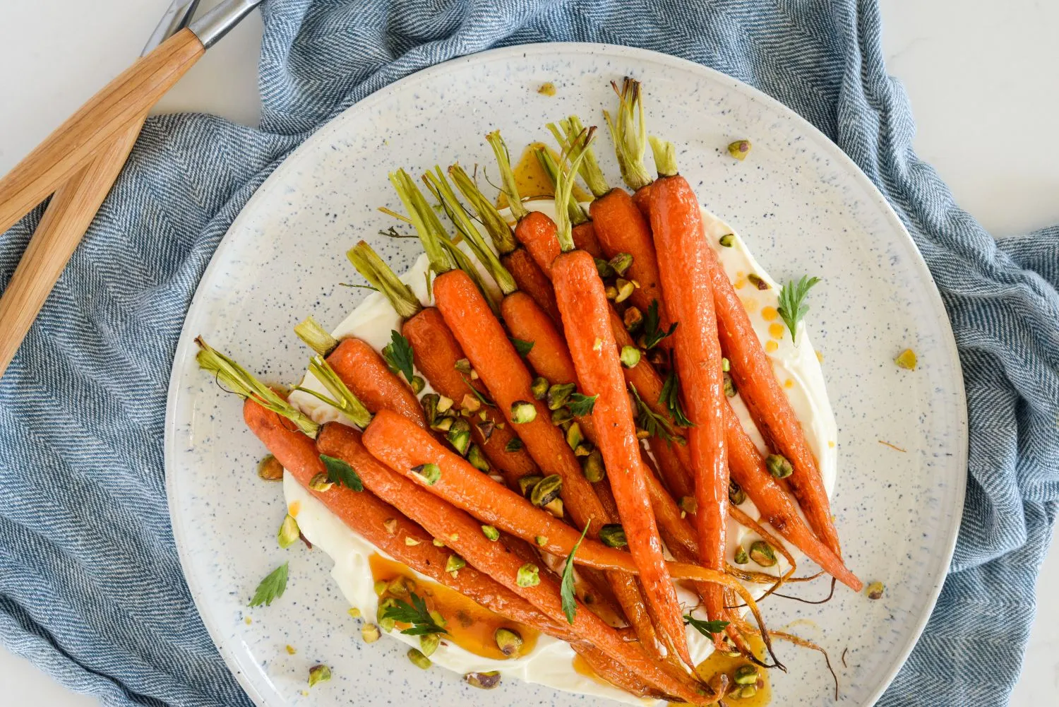 Plated roasted carrots with whipped ricotta and hot honey butter garnished with chopped pistachios, flake salt and pepper, and carrot fronds.