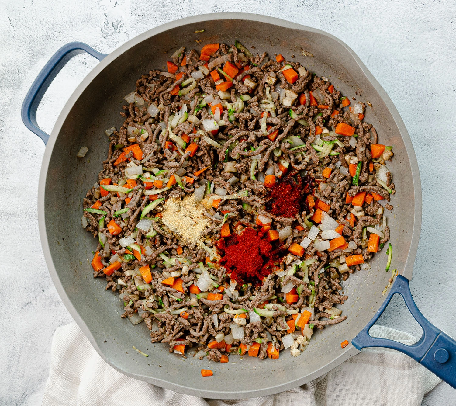 Ground beef, carrots, onion, zucchini, mushrooms topped with fresh seasoning including chili powder, paprika, and garlic powder in a skillet.