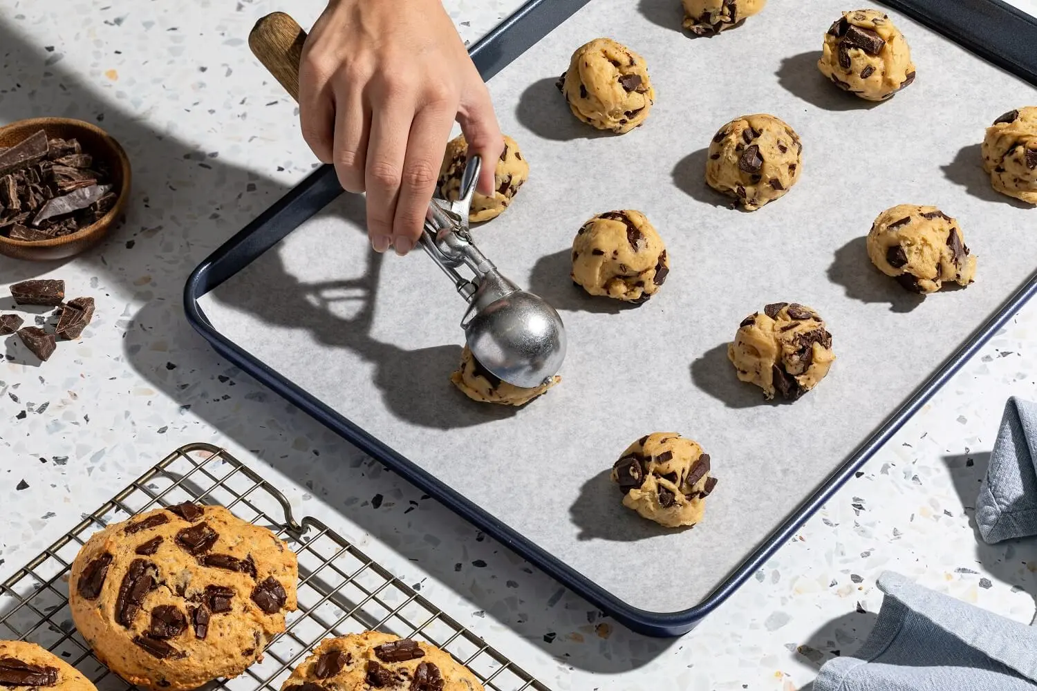 Cookie dough scooped with a portioning tool and placed on a tray lined with wax paper.