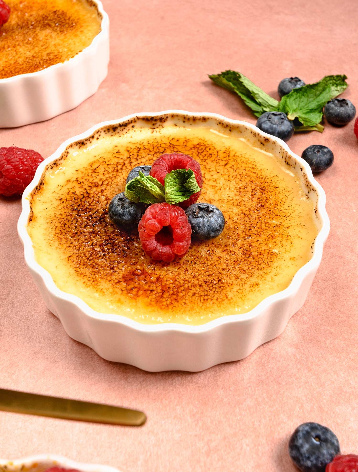 High Protein Greek Yogurt Crème Brûlée served in a ramekin and topped with rasberries and blueberries.