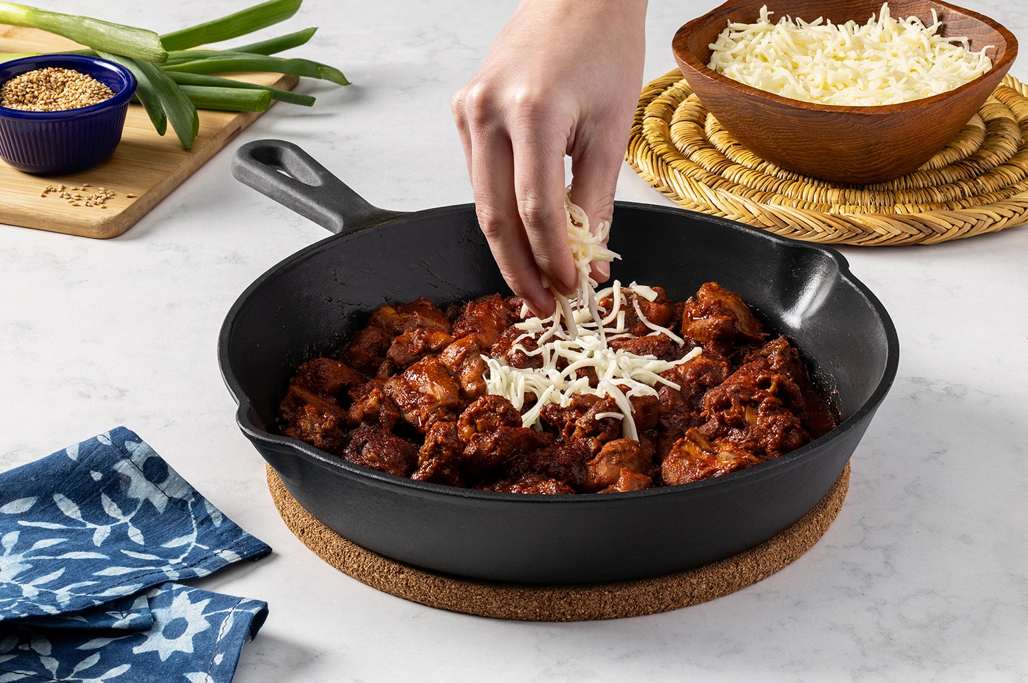 mozzarella cheese sprinkled on top of buldak chicken, cooked in a large cast-iron skillet.