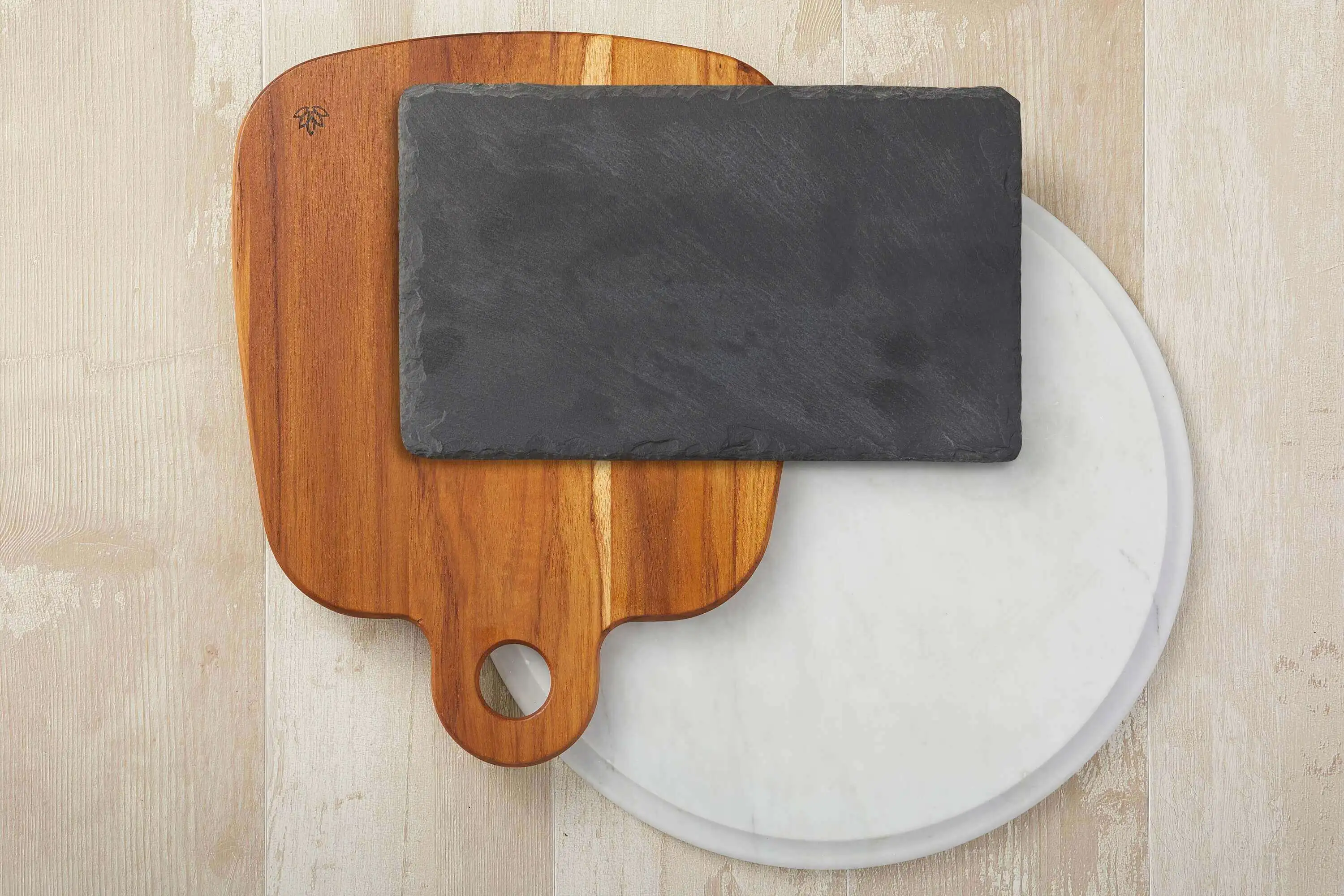 Collection of cheese platter boards made of wood, slate, and marble arranged in a layered pattern, one on top of the other.