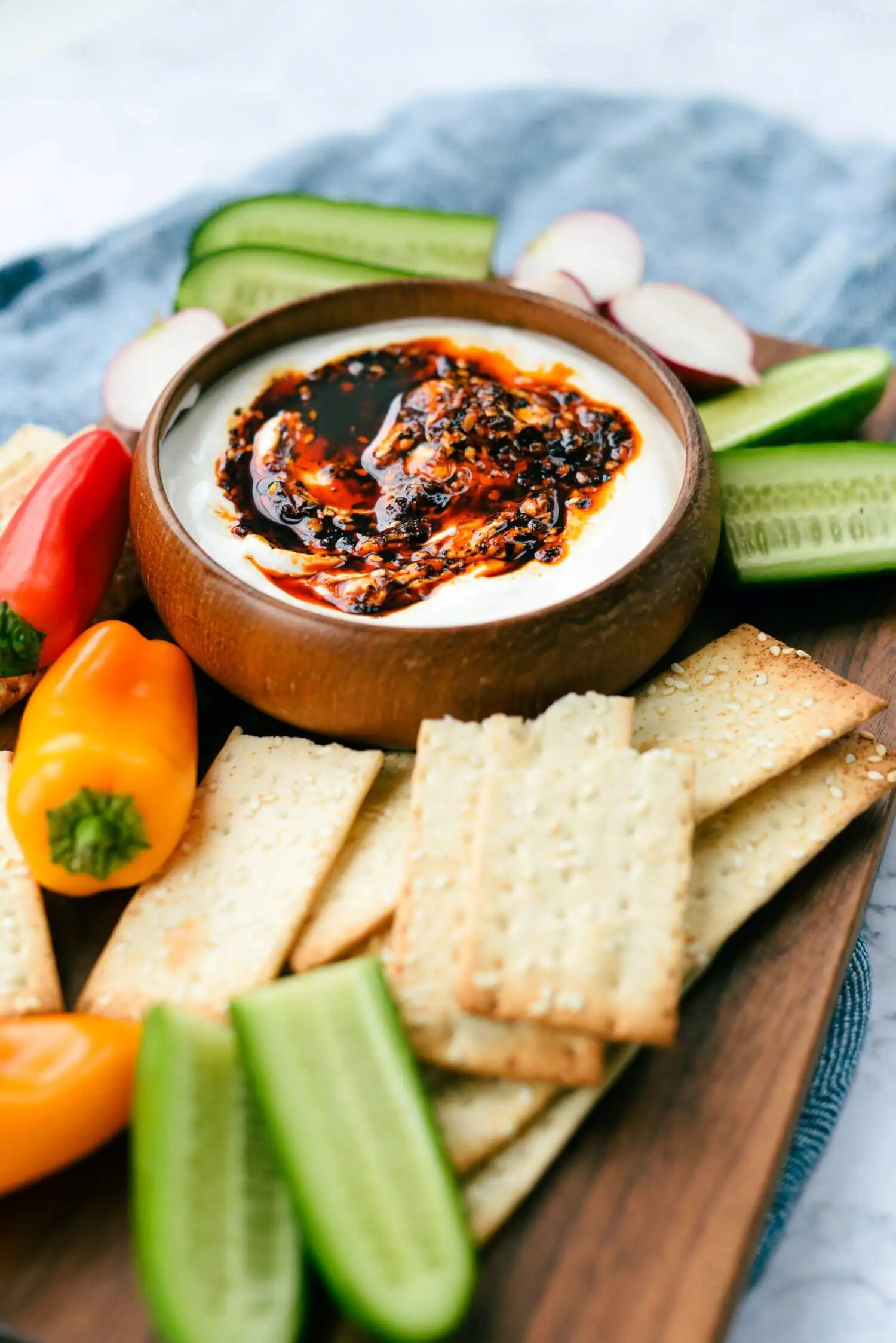 Whipped cottage cheese and chili crisp dip presented on a board with crackers and vegetables.