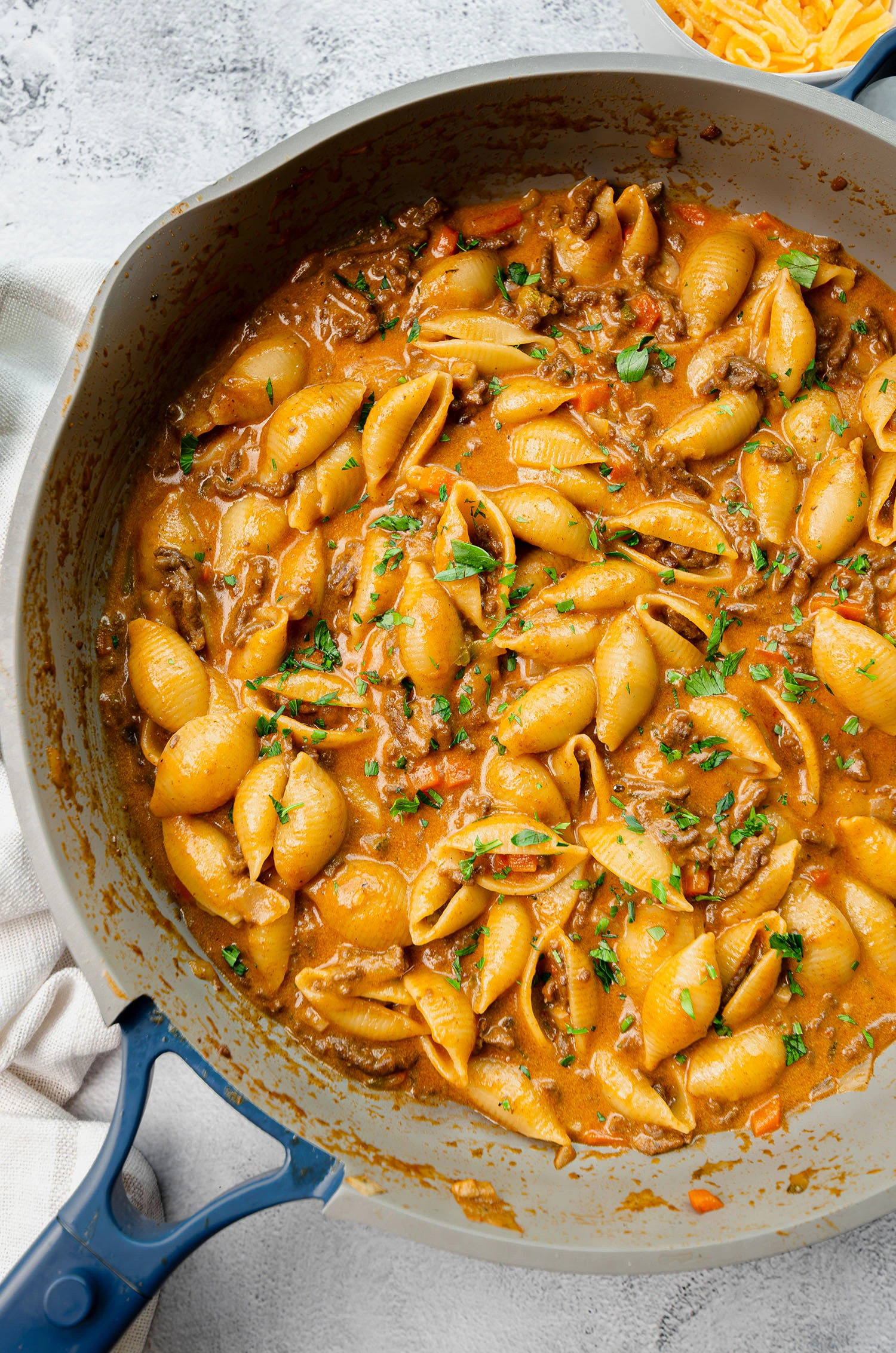A completed hamburger veggie pasta dish featuring ground beef, carrots, onion, mushroom, zucchini, and cheddar cheese in a pan garnished with fresh parsley, ready to be served.