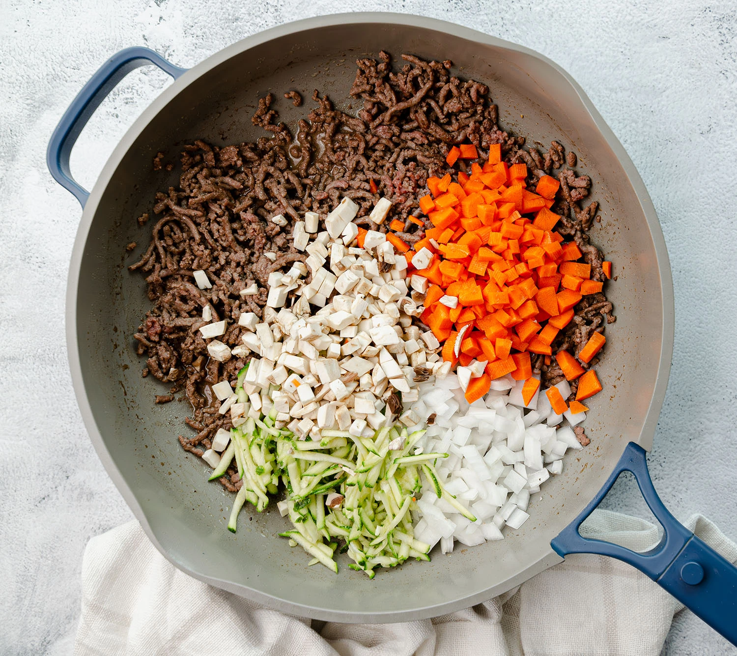 Ingredients for this recipe are chopped and placed in a pan which includes ground beef, carrots, onions, mushrooms, and zucchini
