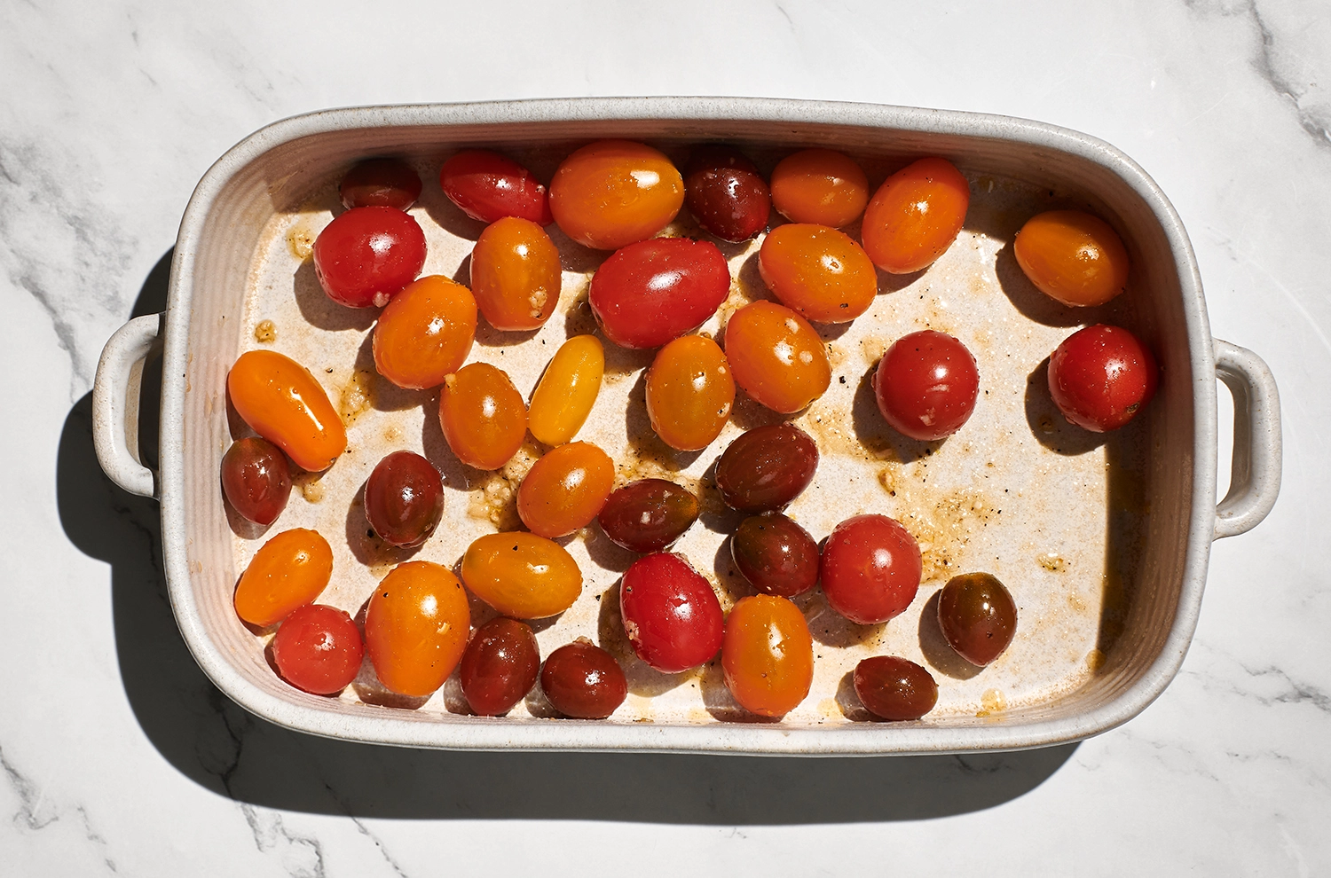 Cherry tomatoes tossed with sea salt, pepper, garlic, and a generous amount of olive oil in a baking dish.
