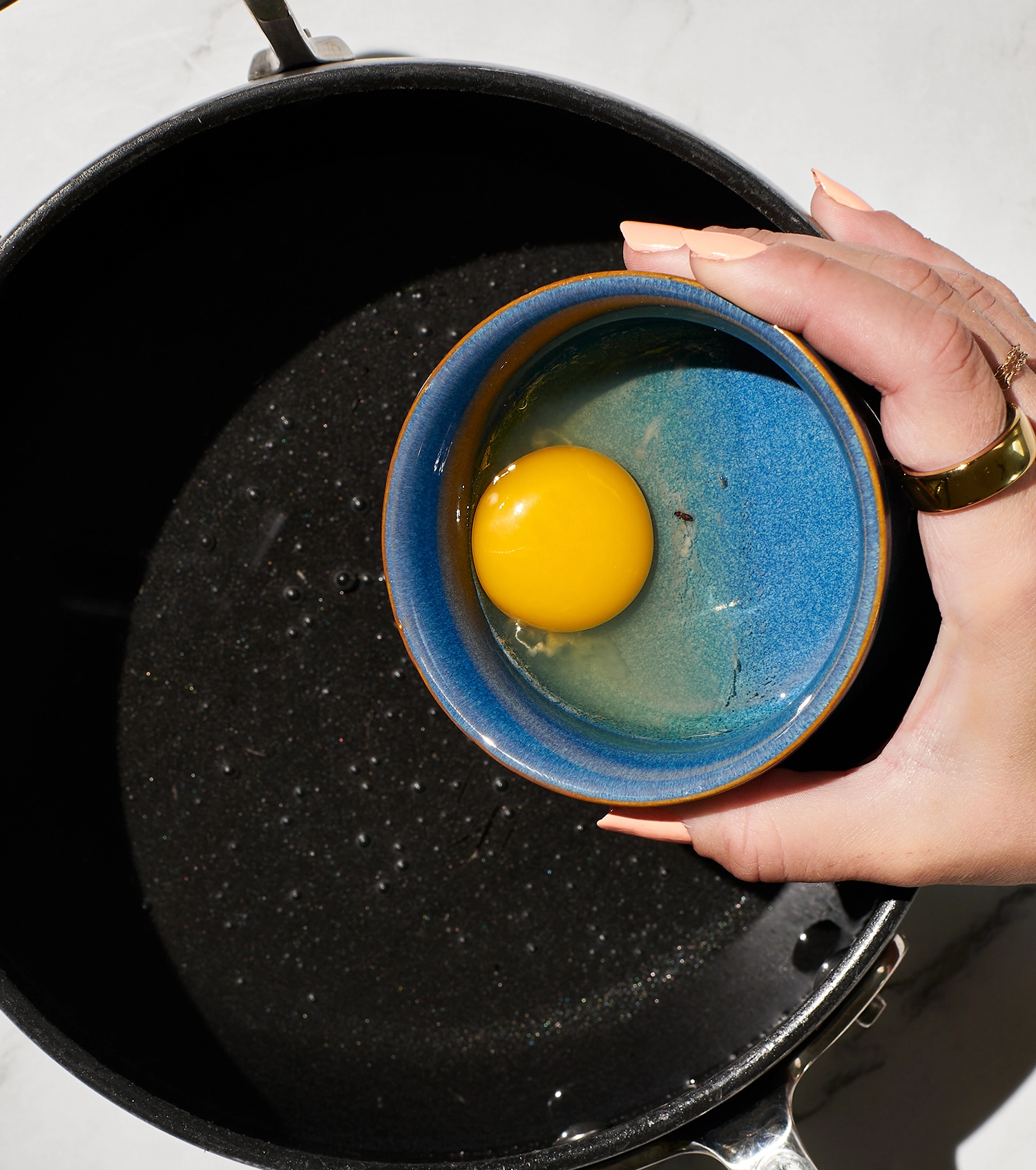 A cracked egg in a small bowl being poured into a gently boiled vortex of salted water and white vinegar in a pot.
