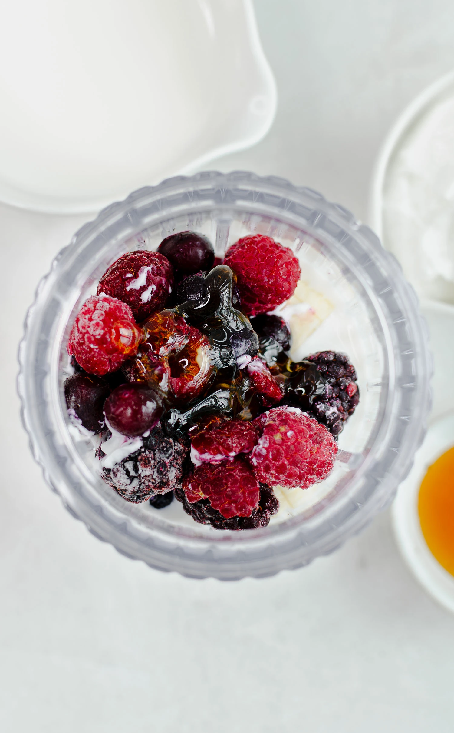 Yogurt, whole milk, honey, and frozen berries including raspberries, blueberries, and blackberries inside of a blender.