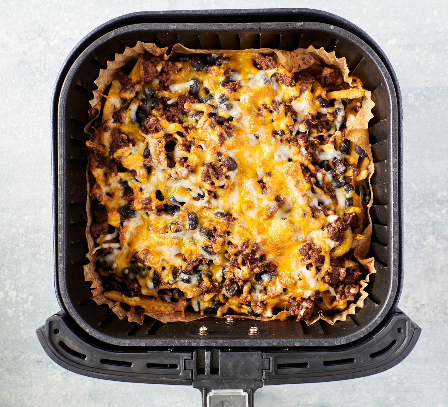 Fries in an air fryer topped with cooked ground beef and melted Mexican cheese.