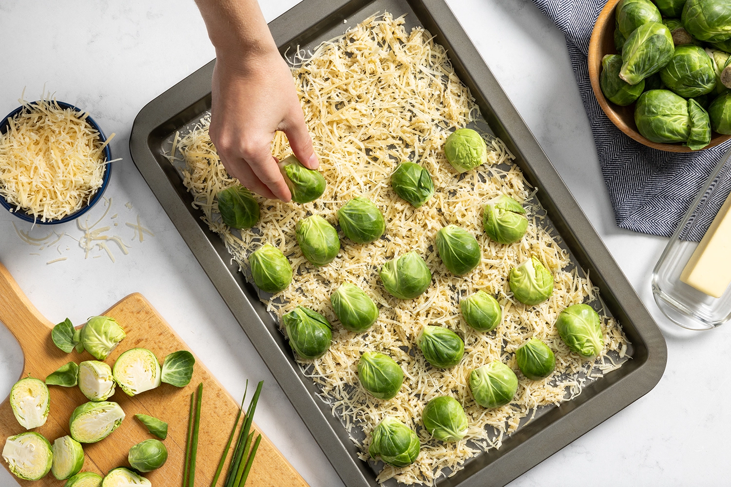A nonstick rimmed baking sheet with a layer of shredded Parmesan cheese and Brussels sprouts cut side down on top of the cheese.