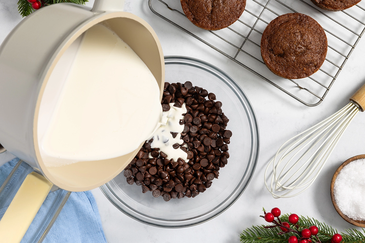Warm cream is poured over chocolate in a glass bowl, then stirred with a spatula until smooth and glossy.