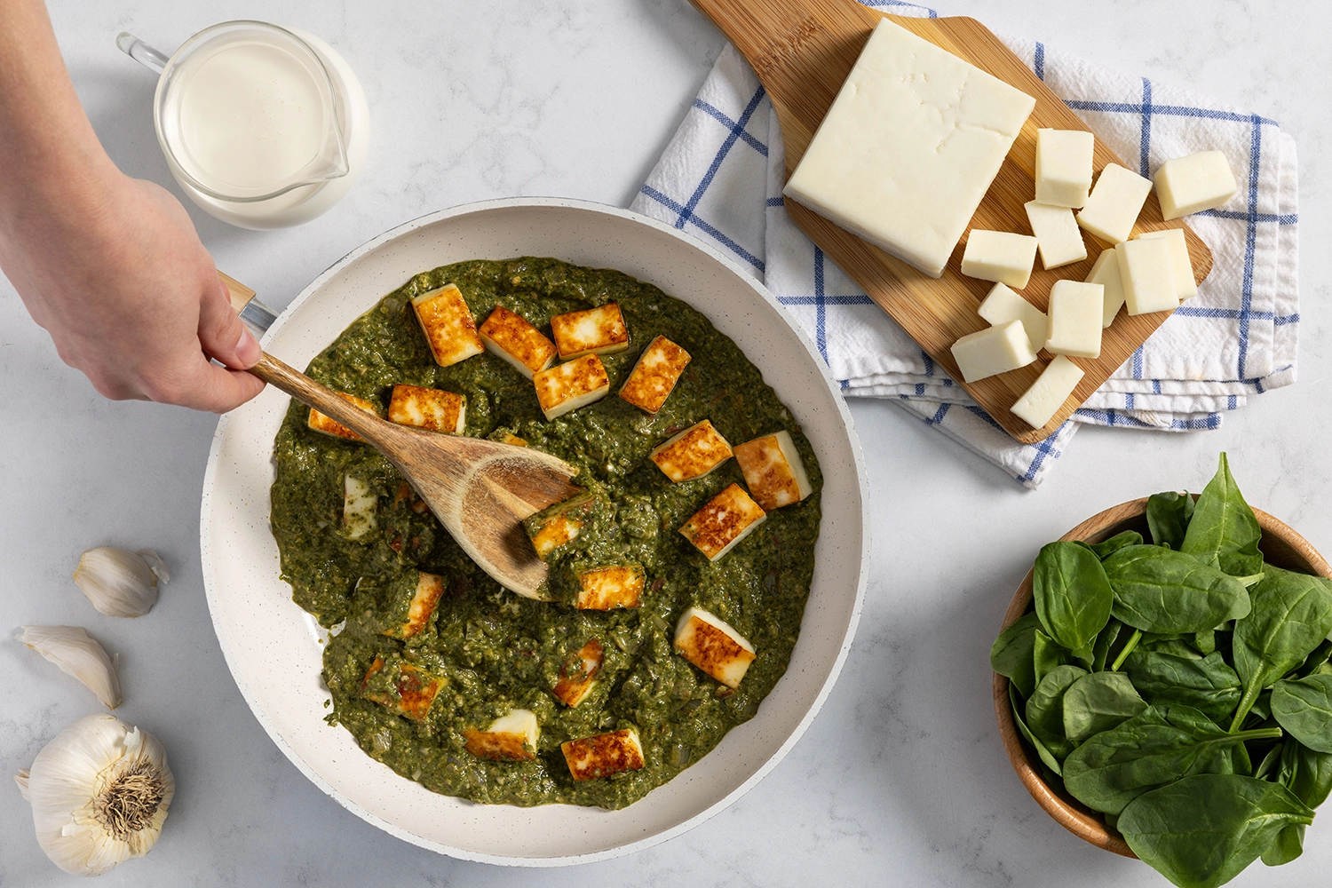Spinach mixture and heavy cream tossed with browned paneer in a skillet.