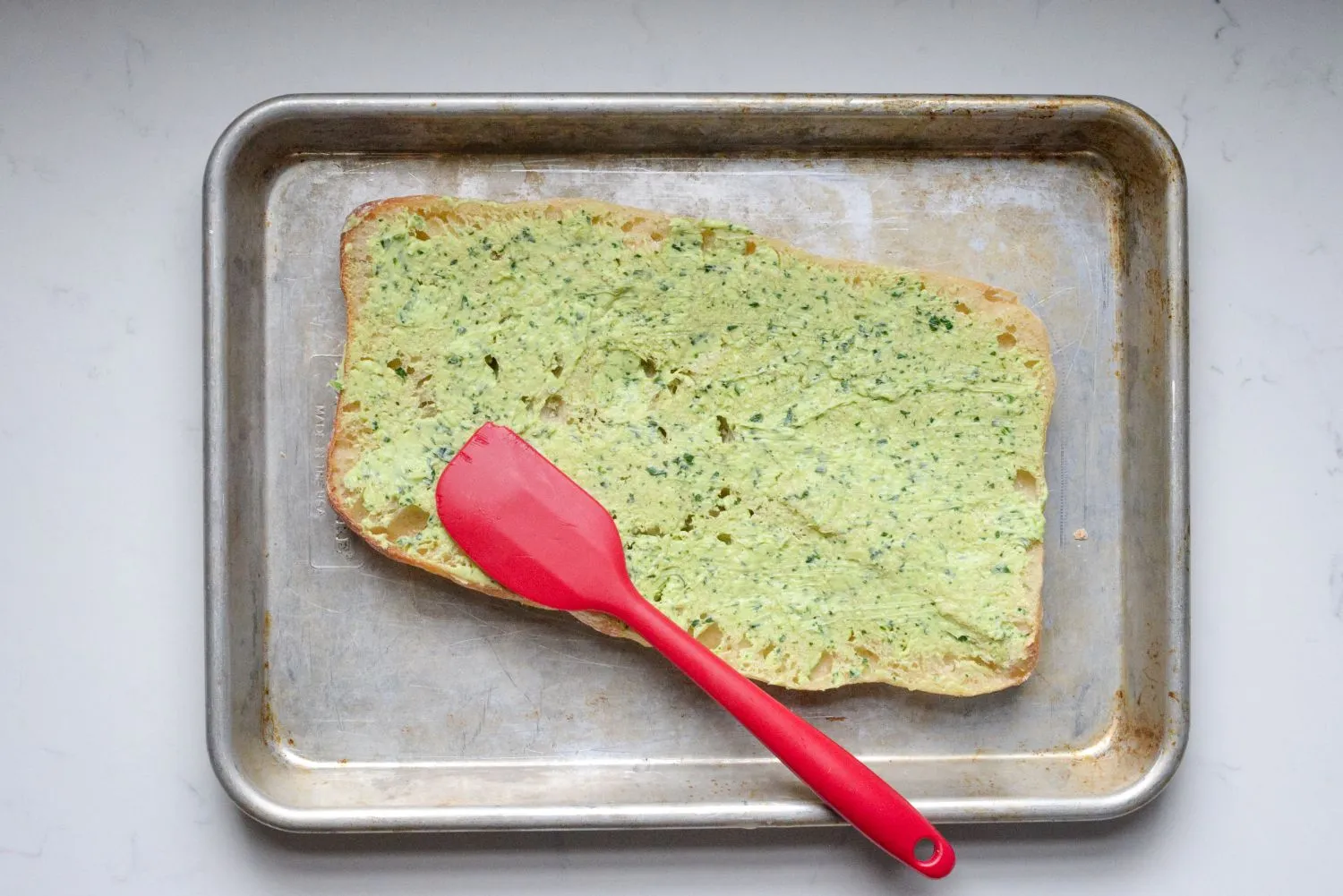 Butter, garlic, and parsley mixture evenly spread over a half slice of Ciabatta bread