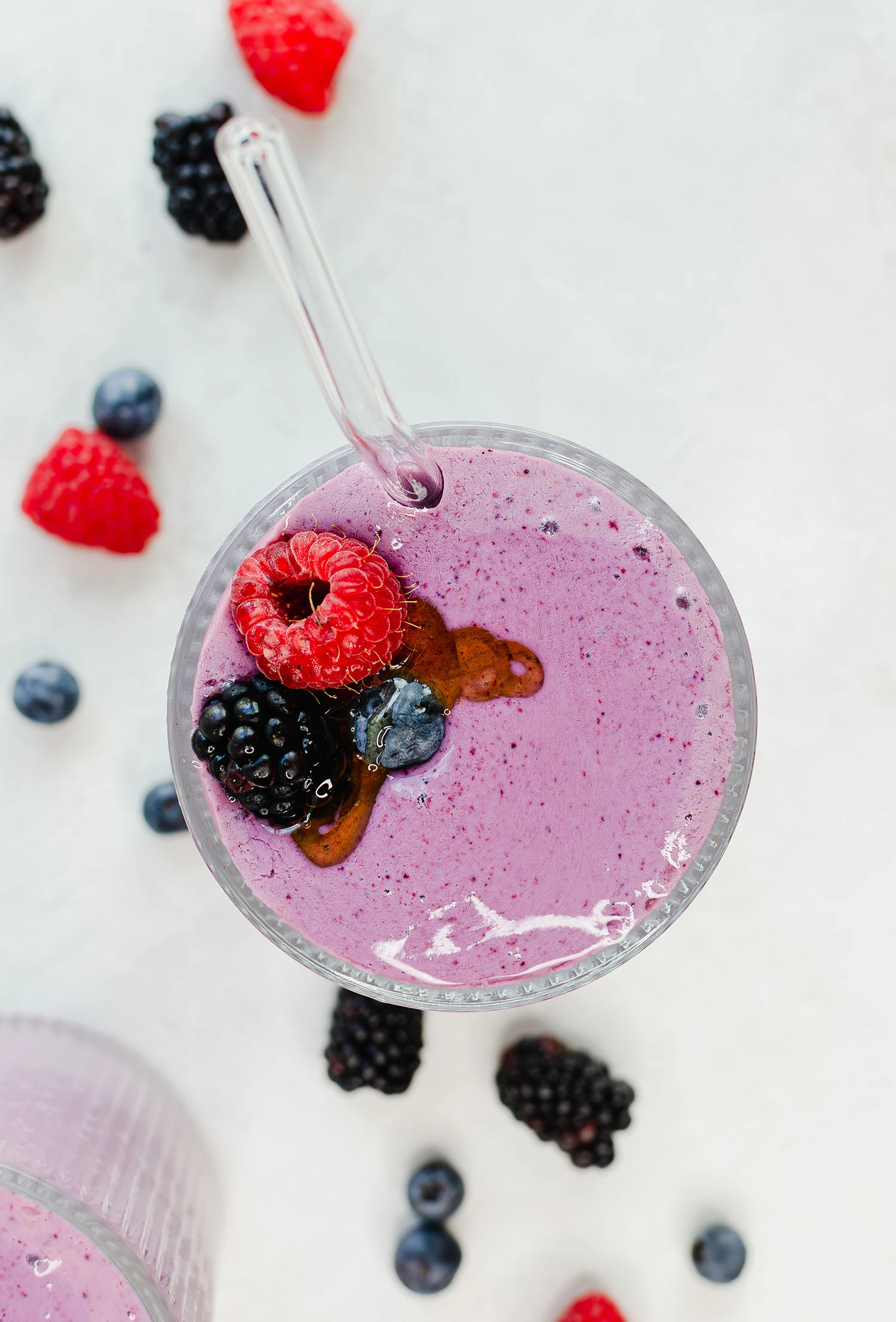 Protein mixed berry smoothie that has been blended inside of a blender with a straw inside, topped with raspberries, blackberries, blueberries, and honey.